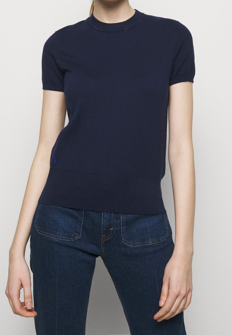 Tmavě modrý svetr s krátkými rukávy a kulatým výstřihem, s texturovaným povrchem a malým vyšitým logem v dolní levé části.