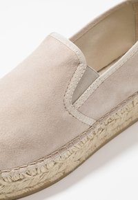 Beżowy zamszowy but wsuwany z plecioną podeszwą z juty. Charakteryzuje się fakturowaną powierzchnią oraz elastycznymi wstawkami po bokach ułatwiającymi zakładanie.