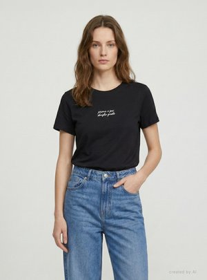 Donna con capelli castano chiaro che indossa una maglietta nera con scritte bianche e jeans blu a vita alta, in piedi davanti a uno sfondo chiaro uniforme.