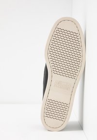 Chancla negra con parte superior sintética texturizada y suela de goma blanca que presenta un patrón de tracción ondulado y logotipos en relieve.