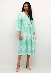 Mint zelena obleka z belimi cvetličnimi vzorci, z gumbi, rokavi do tri četrtine v obliki zvonca in vezava na pasu za prilagodljivost.