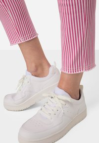 Witte leren sneakers met platte veters, dikke zool en geperforeerde details, gecombineerd met roze en witte gestreepte cropped broeken.