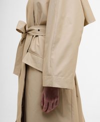 Beige trench coat with a tied waist, featuring a button closure and a pocket detail. Smooth texture and loose fit with wide sleeves.