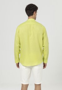 Langsleeve shirt van felgele linnen, met een rugplooitje, knoopmanchetten en een gebogen zoom, gecombineerd met witte shorts.
