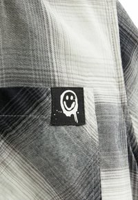 Tissu à carreaux noir et blanc avec une petite pièce noire comportant un logo smiley blanc dégoulinant cousue sur le matériau.