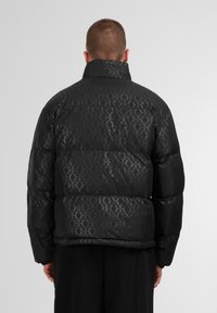 Giacca a vento nera con un motivo sottile, colletto alto e design trapuntato. Il materiale ha una texture lucida con una chiusura a zip nell'orlo.