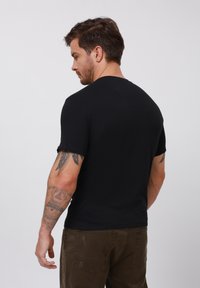 Czarny t-shirt z krótkim rękawem i okrągłym dekoltem. Charakteryzuje się dopasowanym krojem i gładką fakturą. Noszony z brązowymi spodniami z widocznymi kieszeniami.
