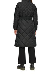 Zwarte gewatteerde lange pufferjas met een getailleerde taille, capuchon en elastische manchetten. De stof heeft een gladde textuur met een ruitpatroon.