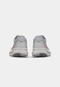 Grijze sneakers met rode accenten, gestructureerde mesh bovenkant, gevoerde zool en rubberen buitenzool. Heeft een low-profile achterkant en een afgeronde neusontwerp.