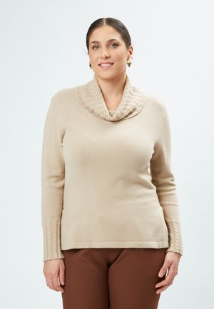 Beige sweater med hætte og ribstrikdetaljer på ærmerne. Blød tekstur og tætsiddende design, parret med brune bukser.