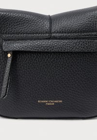 Crna kožna torbica s teksturiranom površinom, preklopnim dizajnom i zlatnim utisnutim logotipom na dnu. Suptilan hardverski detalj sa strane.