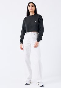 Sudadera negra recortada con mangas largas, pequeño logo en el pecho, combinada con jeans blancos de pierna ancha y cintura alta y zapatillas blancas.