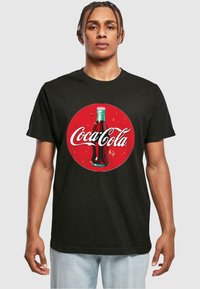 Sort t-shirt med et cirkulært rødt Coca-Cola logo, der har en illustration af en vintage glasflaske samt hvid skrifttype. Casual pasform.