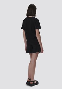 Camiseta de algodón negra combinada con pantalones cortos negros y sandalias negras de suela gruesa. Diseño simple, mangas cortas y corte relajado.