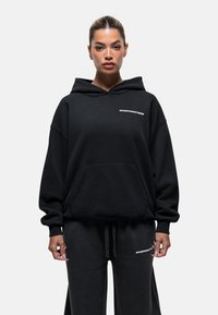 Zwarte hoodie met voorzak, voorzien van de tekst "GOODFORNOTHING" in het wit. Zacht materiaal met een ontspannen pasvorm, gecombineerd met bijpassende broek.