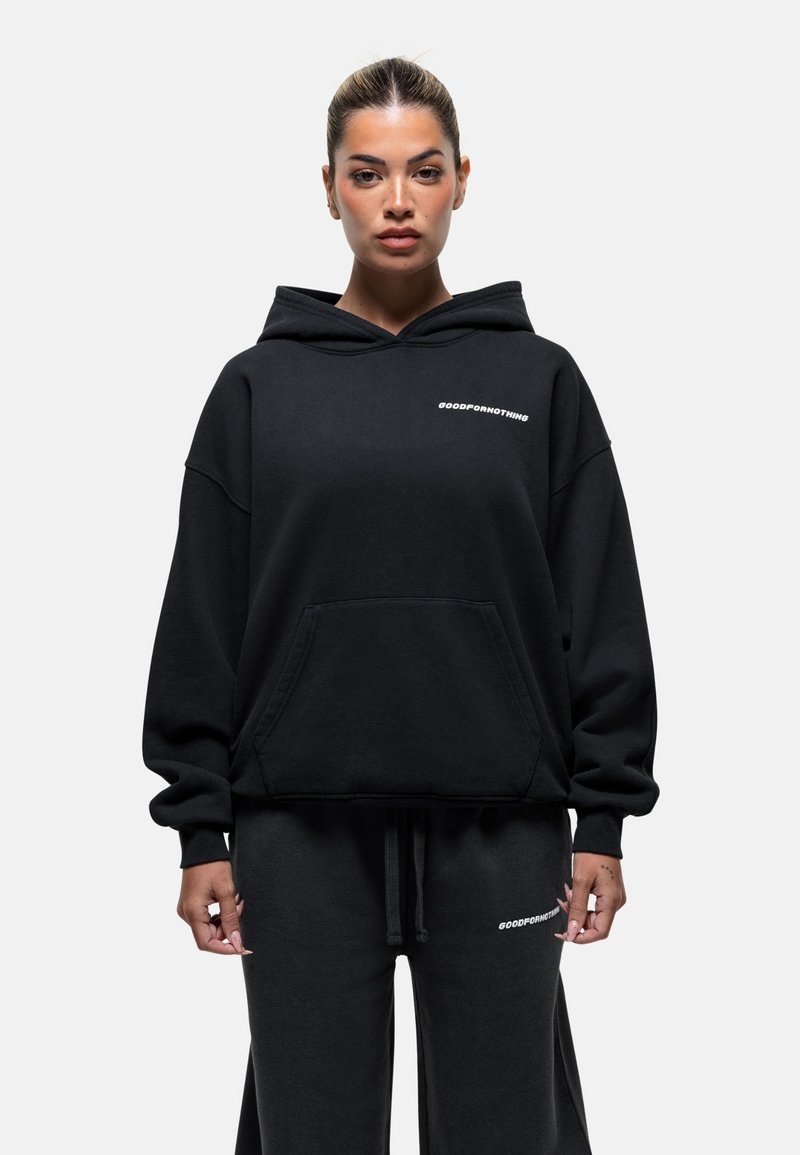 Zwarte hoodie met voorzak, voorzien van de tekst "GOODFORNOTHING" in het wit. Zacht materiaal met een ontspannen pasvorm, gecombineerd met bijpassende broek.