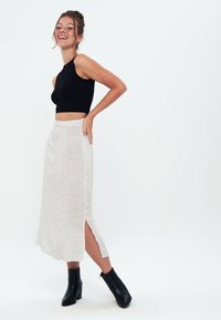 Top crop nero a costine abbinato a una gonna midi bianca con un leggero motivo a pois e spacchi laterali, completato da stivali neri alla caviglia.
