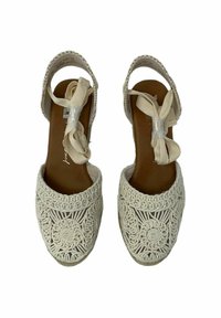 Sandalias de croché blancas con punta cerrada, talón abierto y cintas de tela en el tobillo. Presentan intrincados patrones en espiral en el material superior.