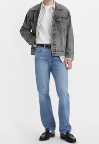 Chaqueta de denim gris, camiseta blanca, camisa a rayas, vaqueros de color azul claro, cinturón negro y mocasines negros. Un atuendo simple y casual con texturas en capas.