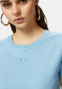 T-shirt in cotone azzurro chiaro con scollatura a girocollo, caratterizzato da un design circolare ricamato con due foglie in azzurro pallido.