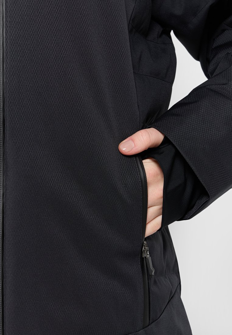 Giacca nera isolata con superficieTexturata, dotata di tasche con zip e silhouette attillata. Primo piano della mano in tasca.