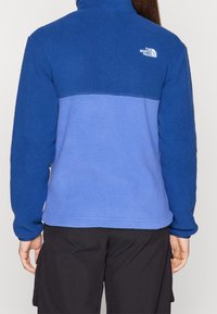 Kurtka polarowa z wysokim kołnierzem, wyróżniająca się niebiesko-niebieskawym wzorem w blokach kolorystycznych. Miękka tekstura z logo na górnej części pleców.