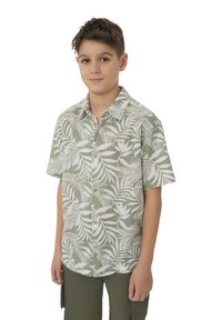 Camicia a maniche corte con bottoni di colore verde chiaro, decorata con motivi a foglia bianchi, realizzata in tessuto traspirante. Indossata con pantaloni cargo color oliva.