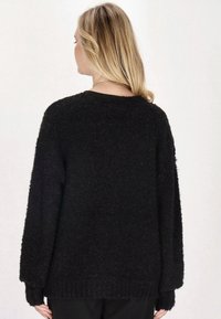 Pulover negru pufos cu o croială lejeră, mâneci largi și tiv cordonat. Textura pare moale și călduroasă, concepută pentru confort și purtare casuală.