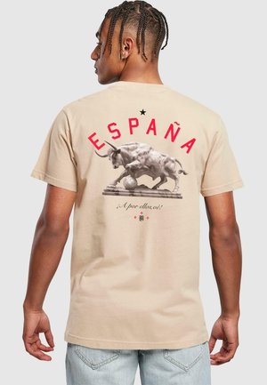 Camiseta de algodón beige con un gran gráfico de un toro y un balón de fútbol en la parte posterior, con "ESPAÑA" impreso en letras rojas en negrita.