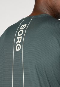 Tume roheline spordisärk, millel on tekstuuritud pind, koos vertikaalse valge triibuga ja sõnaga "BORG", mis on väljapotustatud.