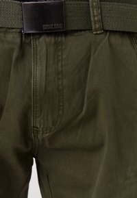 Pantalons vert olive au texture lisse, dotés d'une boucle en métal noir et d'une ceinture tissée. Comprend des coutures visibles et des poches.