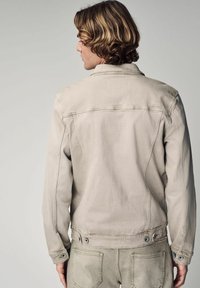 Beige denim jacket met een klassieke kraag, zichtbare naden en drukknopen. Lichte textuur, getailleerd ontwerp en een minimalistische silhouet.