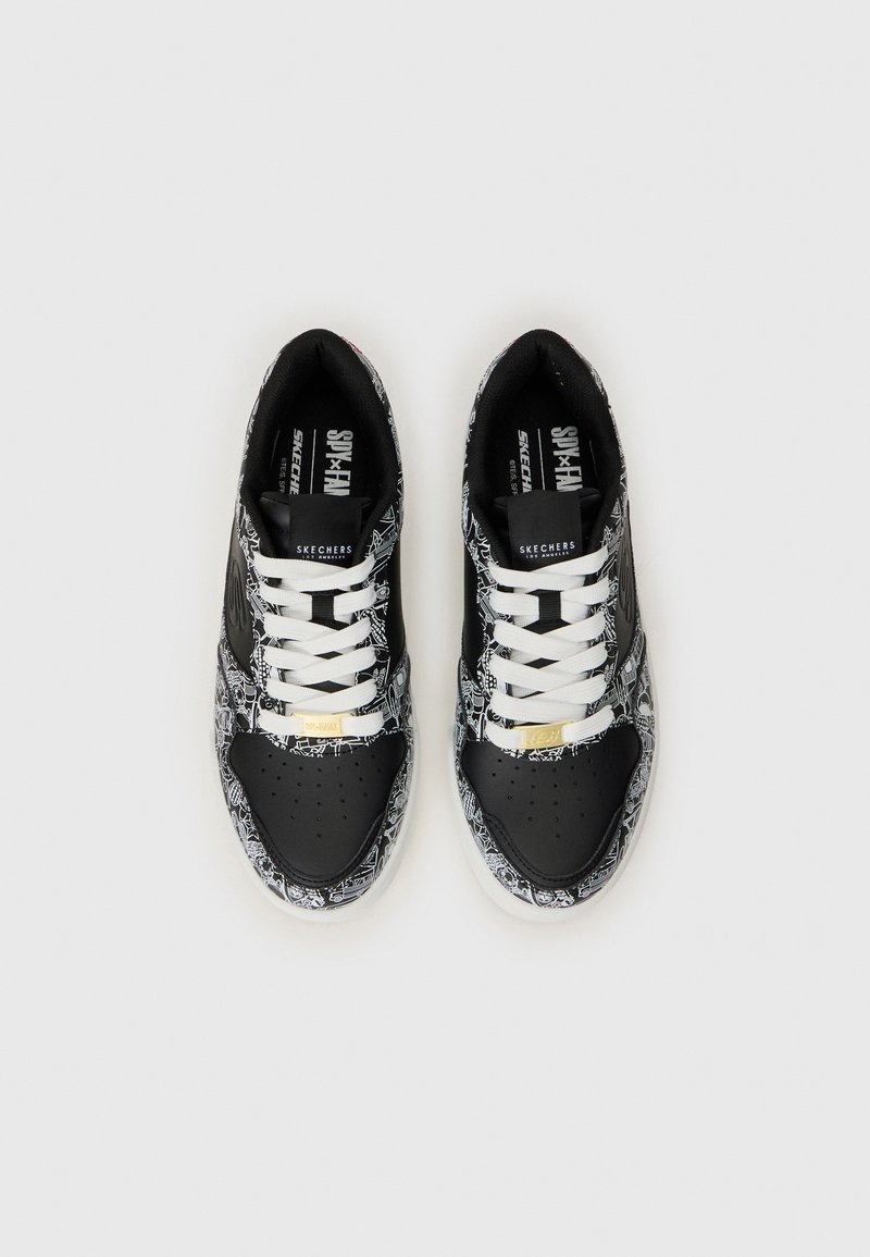 Des baskets noir et blanc avec des motifs complexes, dotées de lacets blancs et d'une touche dorée sur le côté, présentées de dessus sur un fond blanc.