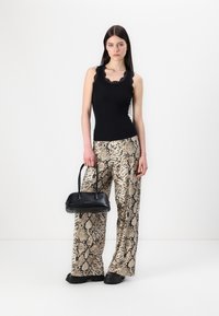 Débardeur noir avec dentelle, associé à un pantalon ample en imprimé serpent beige et un petit sac à main noir. Tissu texturé et design épuré.