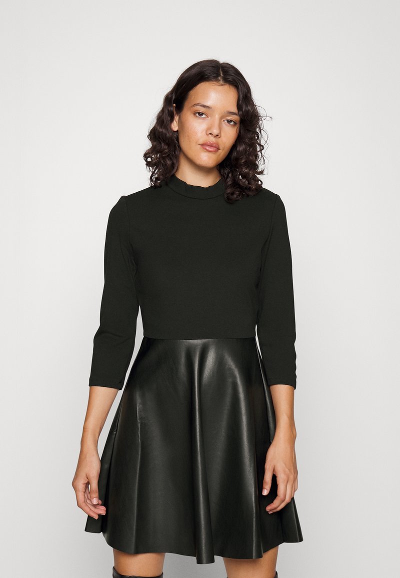 Robe noire mi-longue avec un buste ajusté, un col rond, des manches trois-quarts et une jupe évasée en cuir. Texture lisse.
