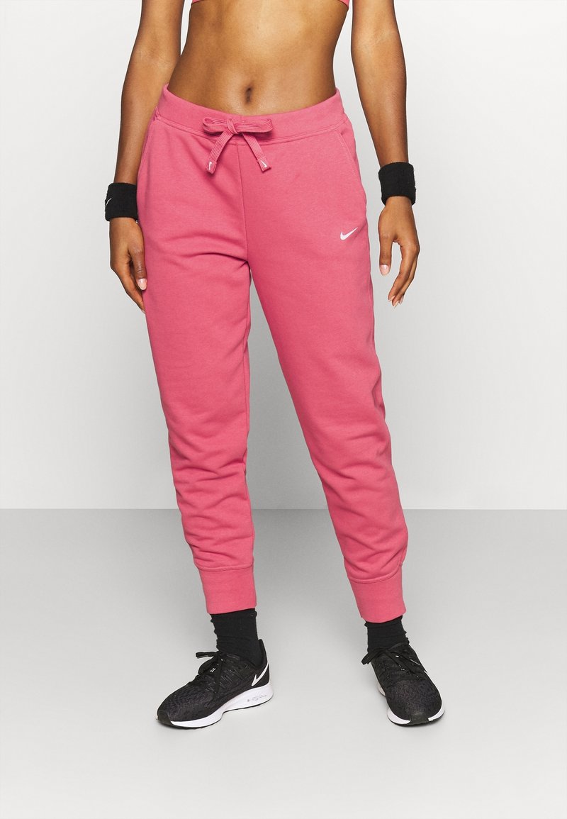 Rosa Baumwoll-Sweatpants mit Kordelzugbund, Bündchen am Knöchel und kleinem weißen Nike-Logo auf der linken Hüfte; getragen mit schwarzen Sportschuhen.