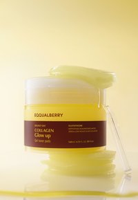 Gul container i plast merket "EQUALBERRY Bouncy Day COLLAGEN Glow Up Gel toner pads," med gelputer delvis synlige ved kanten.