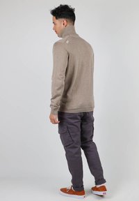 Pull à col montant beige avec des poignets et un ourlet côtelés, associé à un pantalon cargo noir avec des poches latérales et des baskets marron.
