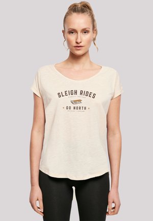 Model wears a light beige T-shirt with "SLEIGH RIDES GO NORTH" printed in dark brown. She stands against a neutral background.