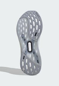 Sottopiede della sneaker con un motivo in gomma testurizzata grigia, sezioni traslucide e molteplici ritagli per la trazione. Accenti neri sono visibili.