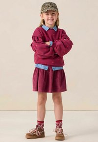 Lila sweatshirt met rode hartpatronen over een denim overhemd met kraag, gecombineerd met een corduroy rok en schoenen en sokken met dierenprint.