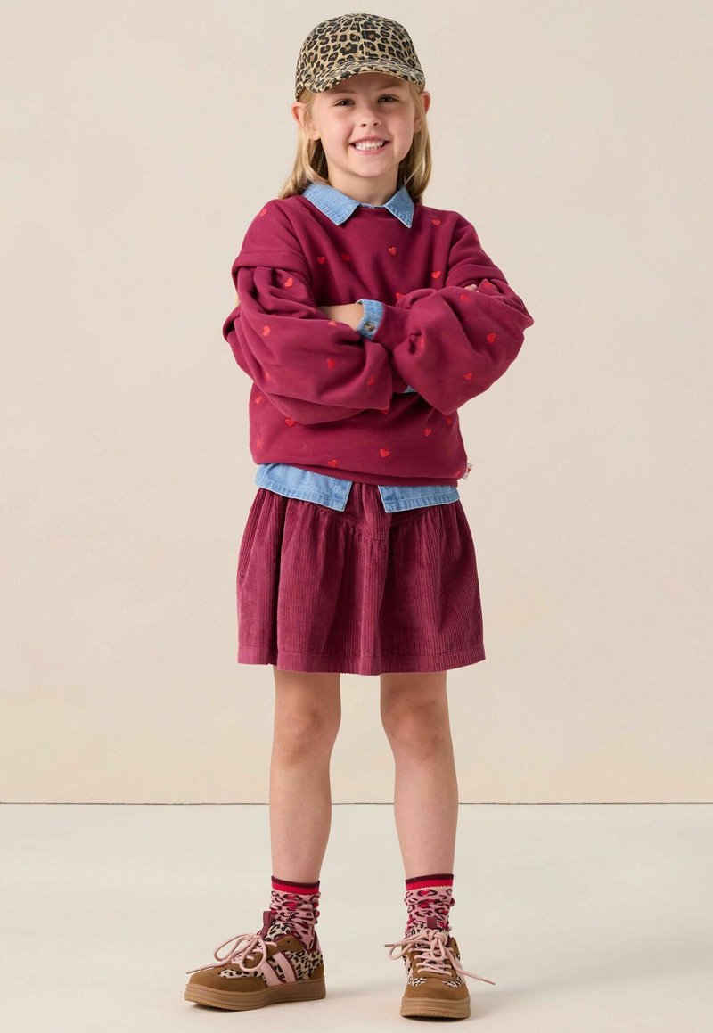 Lila sweatshirt met rode hartpatronen over een denim overhemd met kraag, gecombineerd met een corduroy rok en schoenen en sokken met dierenprint.