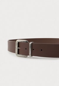 Pruun nahast vöö ruudukujulise, veidi kulunud hõbedase pangedega ja kahe reguleerimisauguga, asetatuna lapikuks heledale taustale.