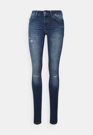 Jeans skinny em denim azul escuro com um acabamento desgastado, apresentando remendos destruidos e um clássico design de cinco bolsos.
