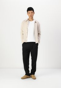 Beige cardigan over a white t-shirt, black trousers, and tan shoes. The cardigan features a collar and button closure. Smooth fabric texture.