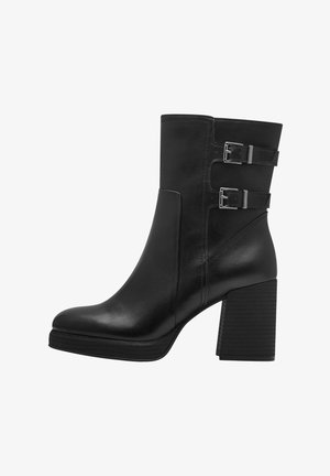 Bottine en cuir noir avec deux accents de boucles en argent, un bout carré et un talon épais empilé. Des panneaux latéraux texturés ajoutent du détail.