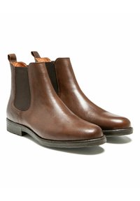 Une paire de bottes Chelsea en cuir marron avec des panneaux élastiques noirs sur les côtés et des tirants, présentées sur un fond blanc.