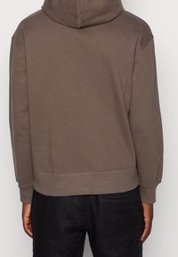 Felpa in cotone marrone con cappuccio regolabile, polsini e orlo a costine. Presenta una vestibilità comoda e un design minimal. Vista posteriore mostrata.