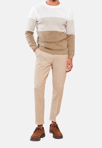 Pull en tricot à rayures crème et beige, pantalon beige cintré, et chaussures marron à lacets avec semelles texturées. Tenue décontractée.