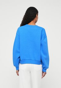 Modrá mikina so spustenými ramenami, rebrovanými manžetami a spodným lemom. Mäkkučká látka, uvoľnený strih, bez viditeľných grafík alebo ozdôb.